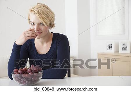 Caucasian woman eating grapes in kitchen View Large Photo Image Stock Photo - Caucasian woman eating grapes in kitchen. Fotosearch