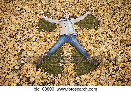 Stock Image - Caucasian woman making angel in autumn leaves. Fotosearch