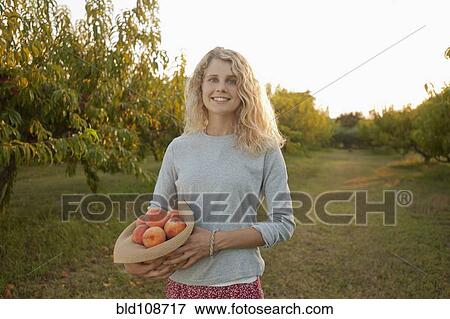 Stock Photo - Caucasian woman picking fruit in orchard. Fotosearch