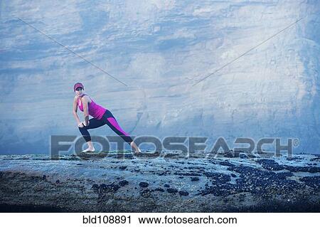 Stock Image - Caucasian woman stretching on rock formations. Fotosearch