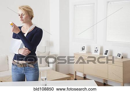 Stock Image - Caucasian woman with broken arm reading pill bottle. Fotosearch