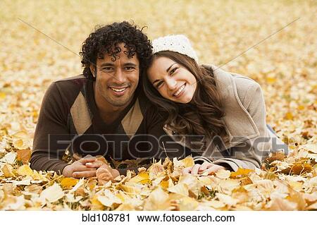 Stock Image - Couple laying in autumn leaves. Fotosearch
