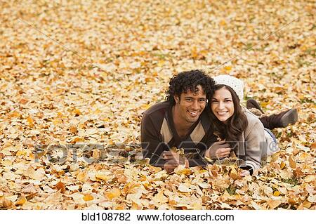 Stock Image - Couple laying in autumn leaves. Fotosearch