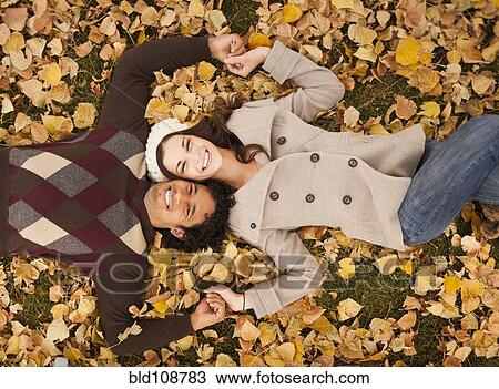 Stock Image - Couple laying in autumn leaves. Fotosearch