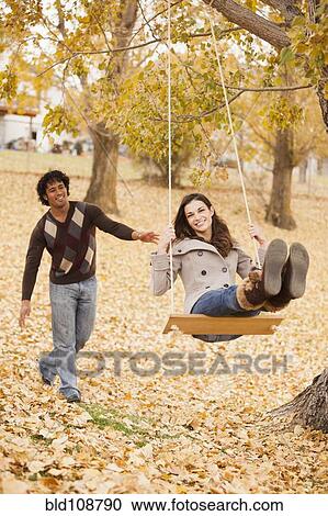 Stock Image - Couple playing on swing in autumn leaves. Fotosearch