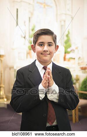 Stock Image - Hispanic boy with hands clasped in church. Fotosearch