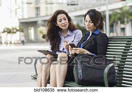Hispanic businesswomen on bench using cell phone and digital tablet View Large Photo Image Stock Photography - Hispanic businesswomen on bench using cell phone and digital tablet. Fotosearch