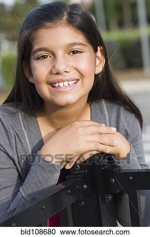 Stock Image - Hispanic girl leaning on metal railing. Fotosearch