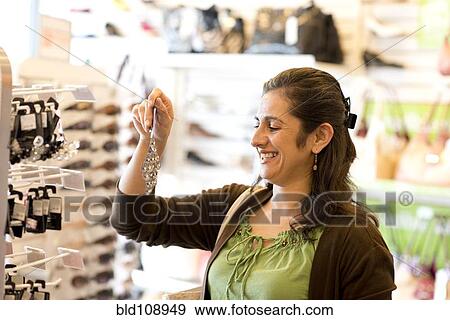Stock Photo - Hispanic woman buying earrings in store. Fotosearch