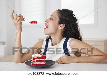 Stock Image - Hispanic woman eating cake in kitchen. Fotosearch
