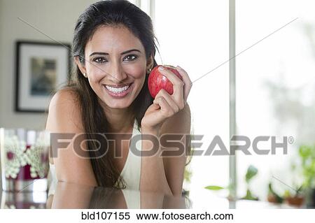 Indian woman holding apple in kitchen View Large Photo Image Stock Photography - Indian woman holding apple in kitchen. Fotosearch