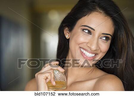 Stock Image - Indian woman spraying perfume on neck. Fotosearch