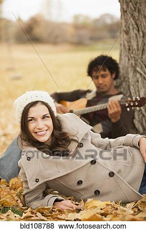 Stock Photo - Man playing guitar for girlfriend in autumn leaves. Fotosearch