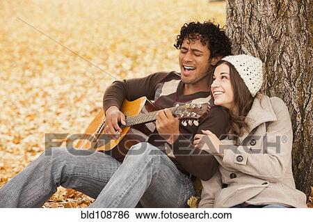 Stock Photograph - Man playing guitar for girlfriend in autumn leaves. Fotosearch