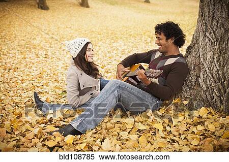 Stock Photography - Man playing guitar for girlfriend in autumn leaves. Fotosearch