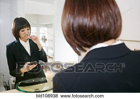 Stock Photo - Mixed race businesswoman checking cell phone in bathroom. Fotosearch