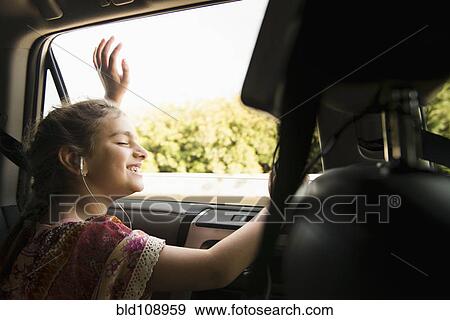 Stock Photo - Mixed race girl listening to headphones in car. Fotosearch