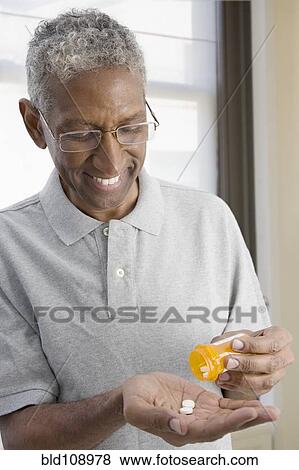 Mixed race man shaking pills from bottle View Large Photo Image Stock Photo - Mixed race man shaking pills from bottle. Fotosearch