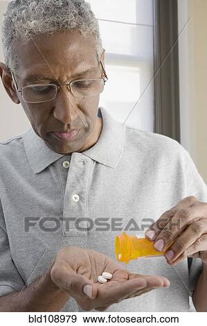 Stock Photo - Mixed race man shaking pills from bottle. Fotosearch
