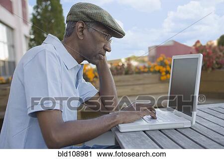 Stock Image - Mixed race man using laptop outdoors. Fotosearch