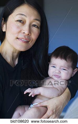 Stock Image - Mother holding baby on bed. Fotosearch