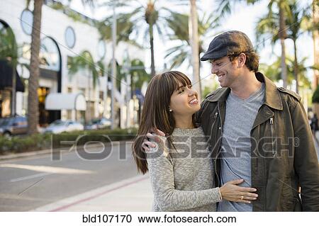 Stock Image - Smiling couple walking on city street. Fotosearch