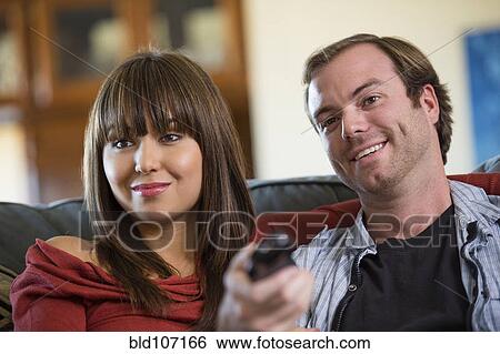 Stock Photograph - Smiling couple watching television on sofa. Fotosearch