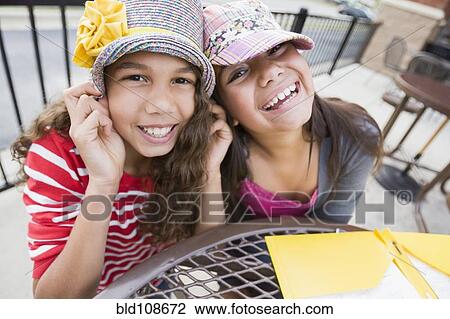 Stock Image - Smiling girls wearing hats at table. Fotosearch