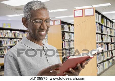 Stock Photography - Smiling mixed race man reading in library. Fotosearch