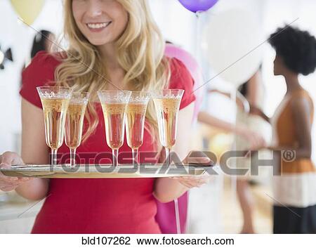 Stock Image - Smiling woman carrying tray of champagne. Fotosearch