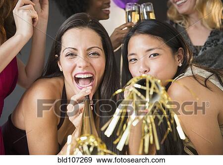 Stock Photo - Smiling women blowing party horns at party. Fotosearch