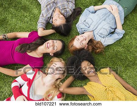 Stock Image - Smiling women laying in grass together. Fotosearch
