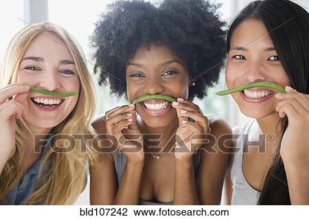Stock Image - Smiling women using green beans as mustaches. Fotosearch