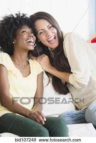 Stock Photo - Women laughing together on sofa. Fotosearch
