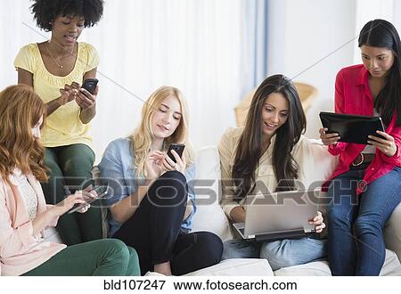 Stock Photo - Women using technology on sofa. Fotosearch