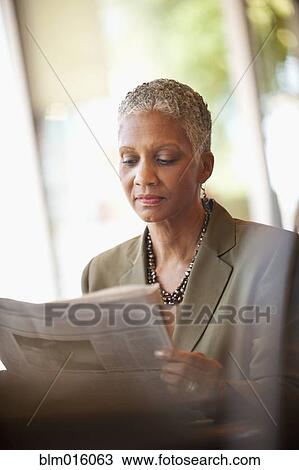Stock Image - African American businesswoman reading newspaper in cafe. Fotosearch