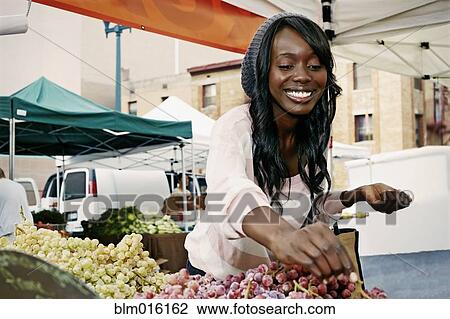 Stock Image - African American woman buying grapes. Fotosearch