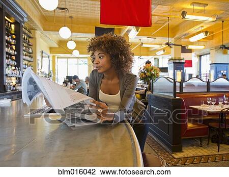 Stock Image - African American woman reading newspaper in cafe. Fotosearch
