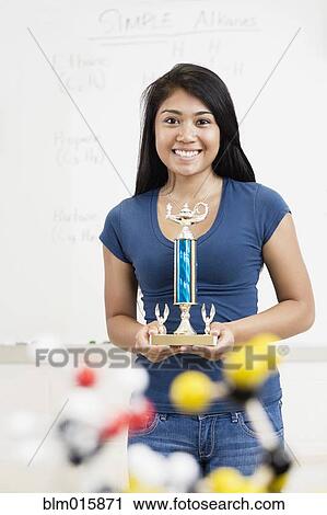 Stock Image - Asian high school student holding trophy in classroom. Fotosearch