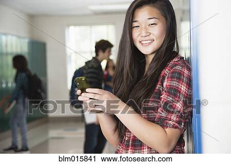 Stock Image - Asian high school student text messaging on cell phone. Fotosearch