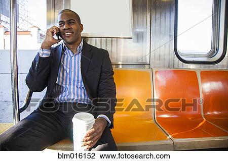 Stock Image - Black businessman talking on cell phone and riding commuter train. Fotosearch