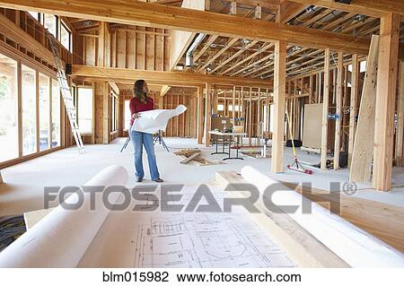 Stock Image - Black construction worker looking at blueprints in unfinished room. Fotosearch