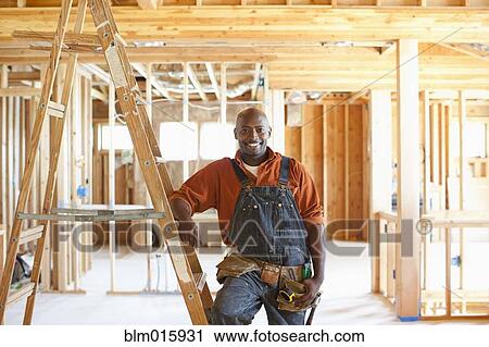 Stock Image - Black construction worker standing in unfinished room. Fotosearch