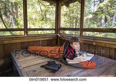 Stock Image - Caucasian boy reading in sleeping bag. Fotosearch