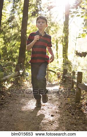 Stock Image - Caucasian boy running on path in forest. Fotosearch