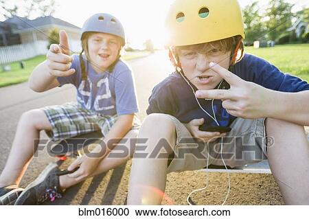 Stock Image - Caucasian boys sitting on skateboards and making gestures. Fotosearch