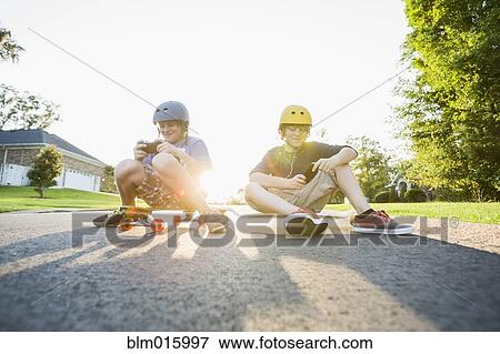 Stock Photo - Caucasian boys sitting on skateboards and using cell phones. Fotosearch
