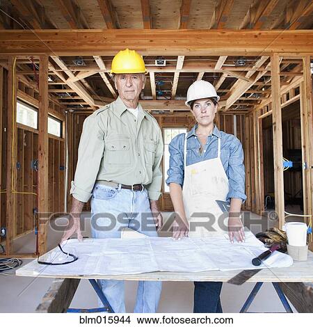 Caucasian construction workers looking at blueprints in unfinished room View Large Photo Image Picture - Caucasian construction workers looking at blueprints in unfinished room. Fotosearch