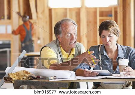 Stock Photo - Caucasian construction workers looking at digital tablet in unfinished room. Fotosearch
