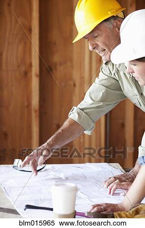 Stock Photography - Caucasian construction workers looking at blueprints in unfinished room. Fotosearch